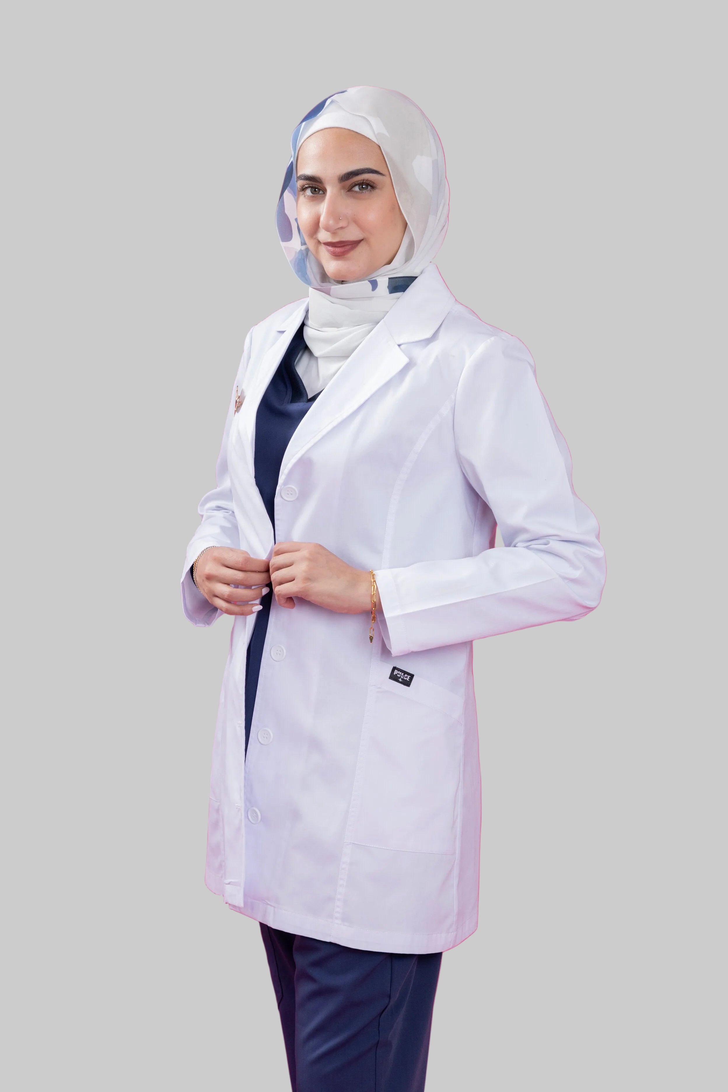 Person wearing a white lab coat and hijab on a pink background