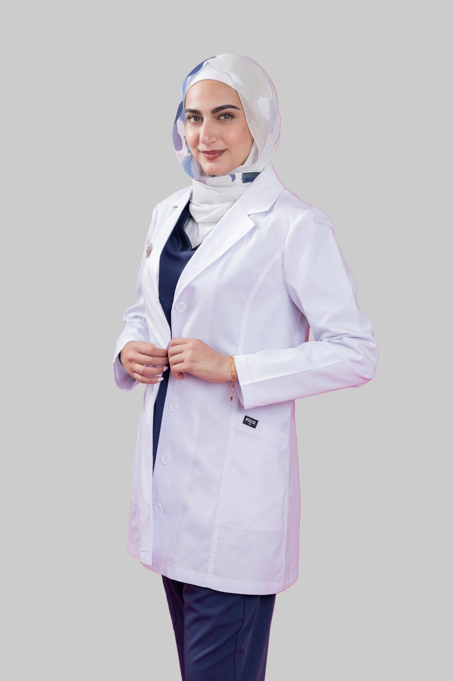 Person wearing a white lab coat and hijab on a pink background