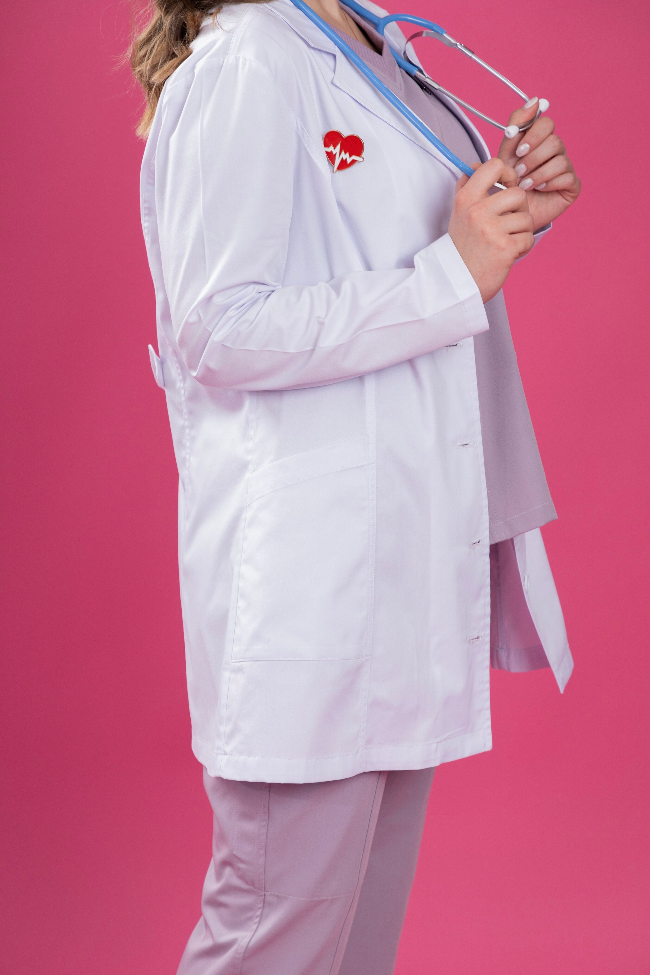 Person wearing a white lab coat with a red heart logo on a pink background