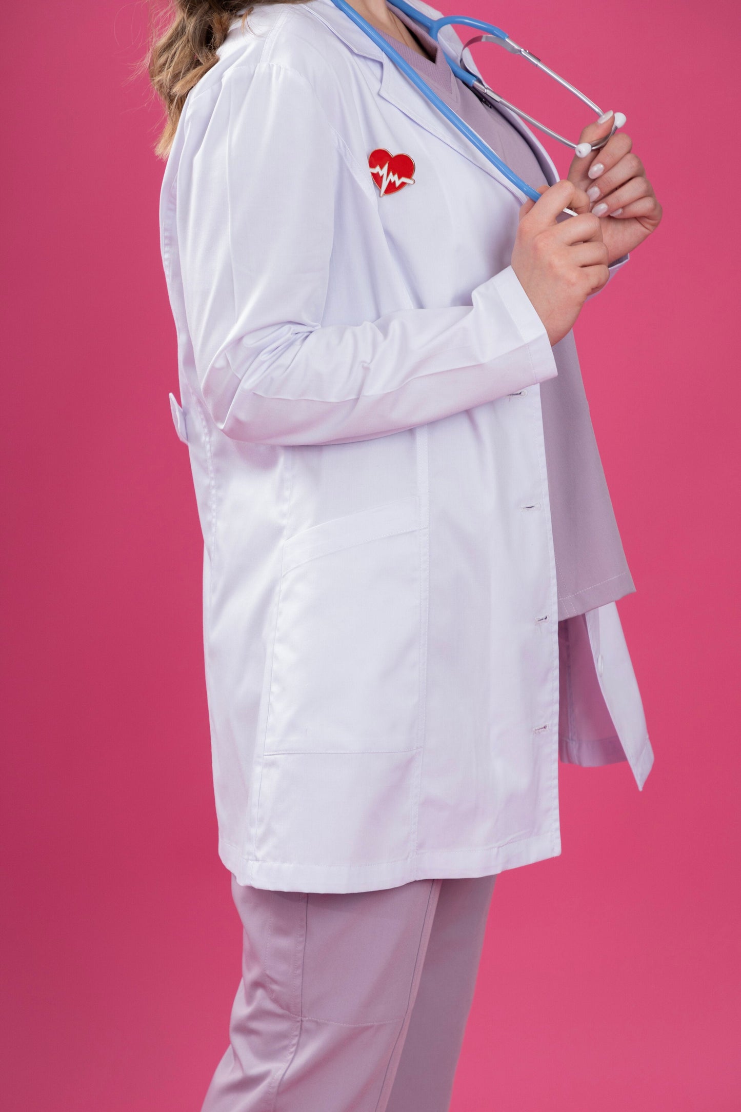 Person wearing a white lab coat with a red heart logo on a pink background