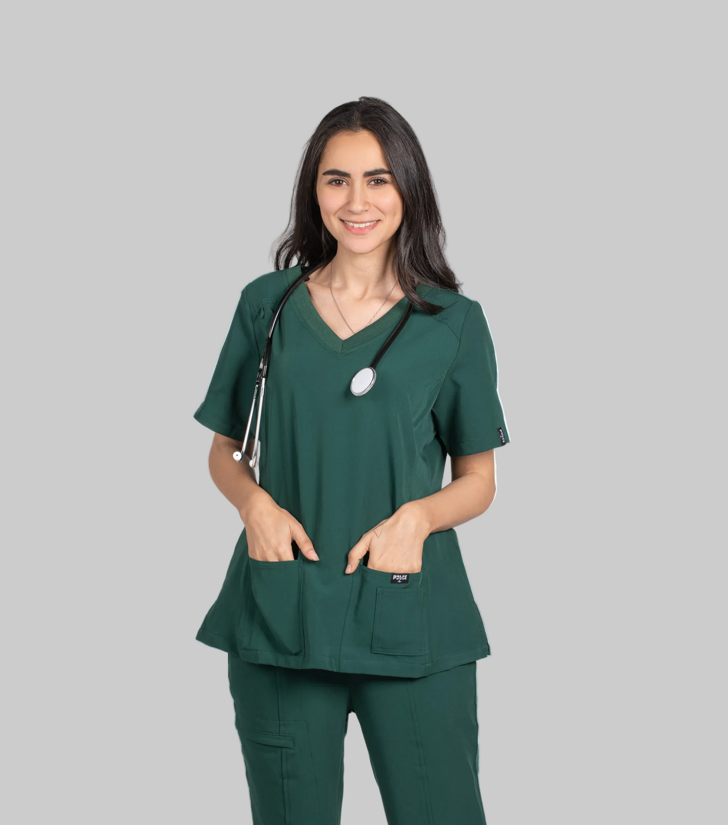 Woman wearing green medical scrubs with a stethoscope, branded 'Pulse', on a white background.